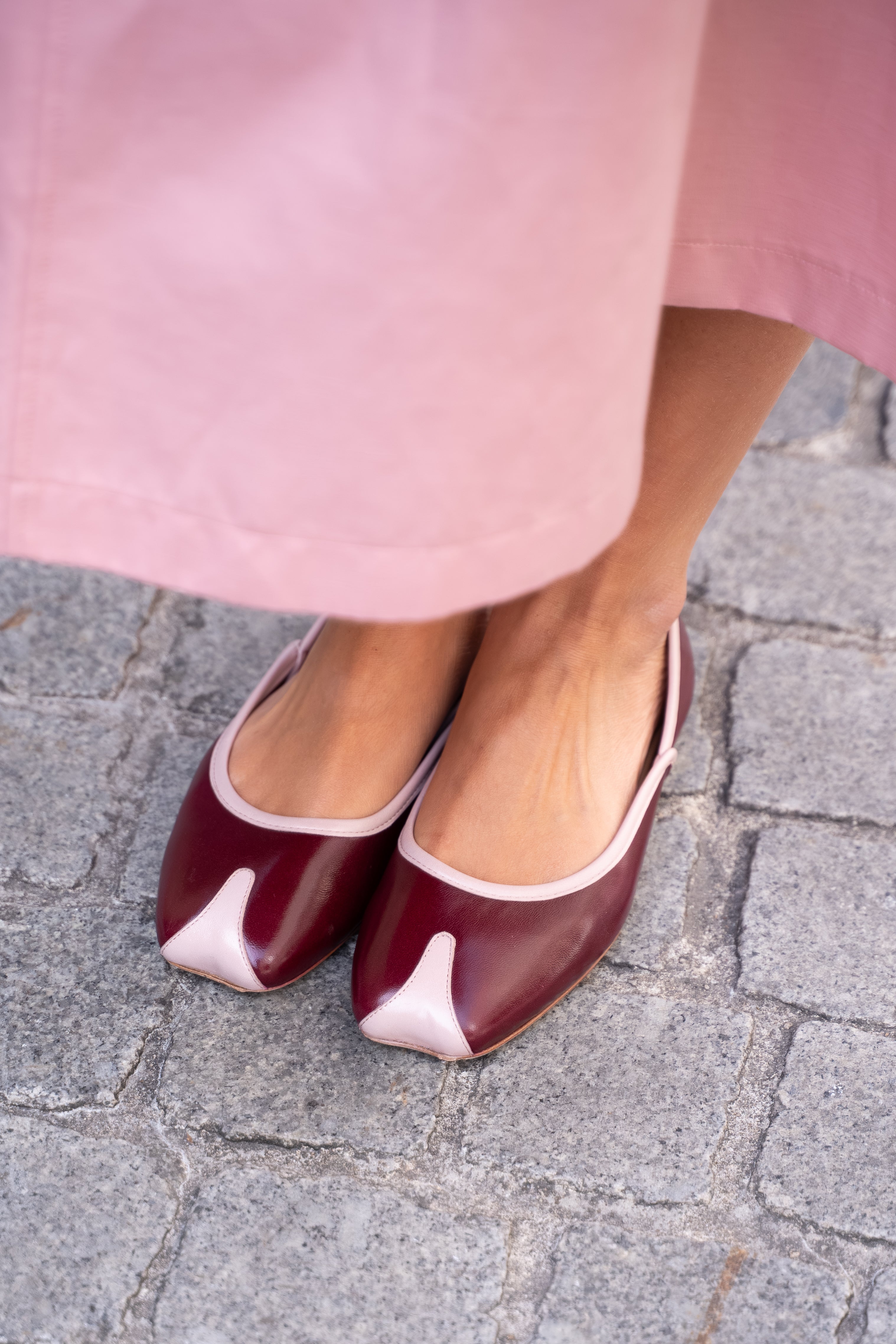 Burgundy shoes with pink accents worn on a stone pavement