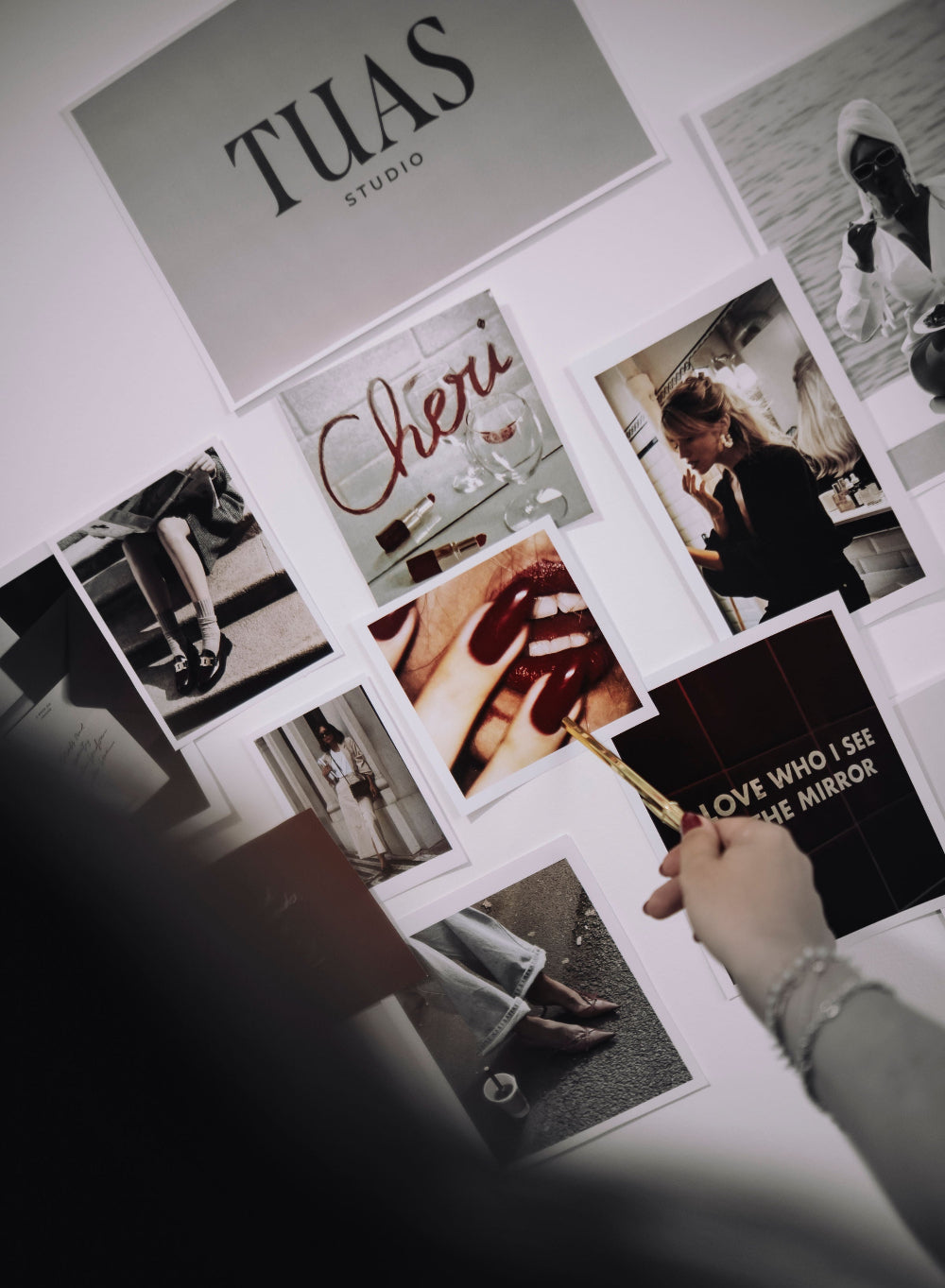 Collage of photos and text on a wall with a hand holding a book titled 'Over I See the Mirror'.