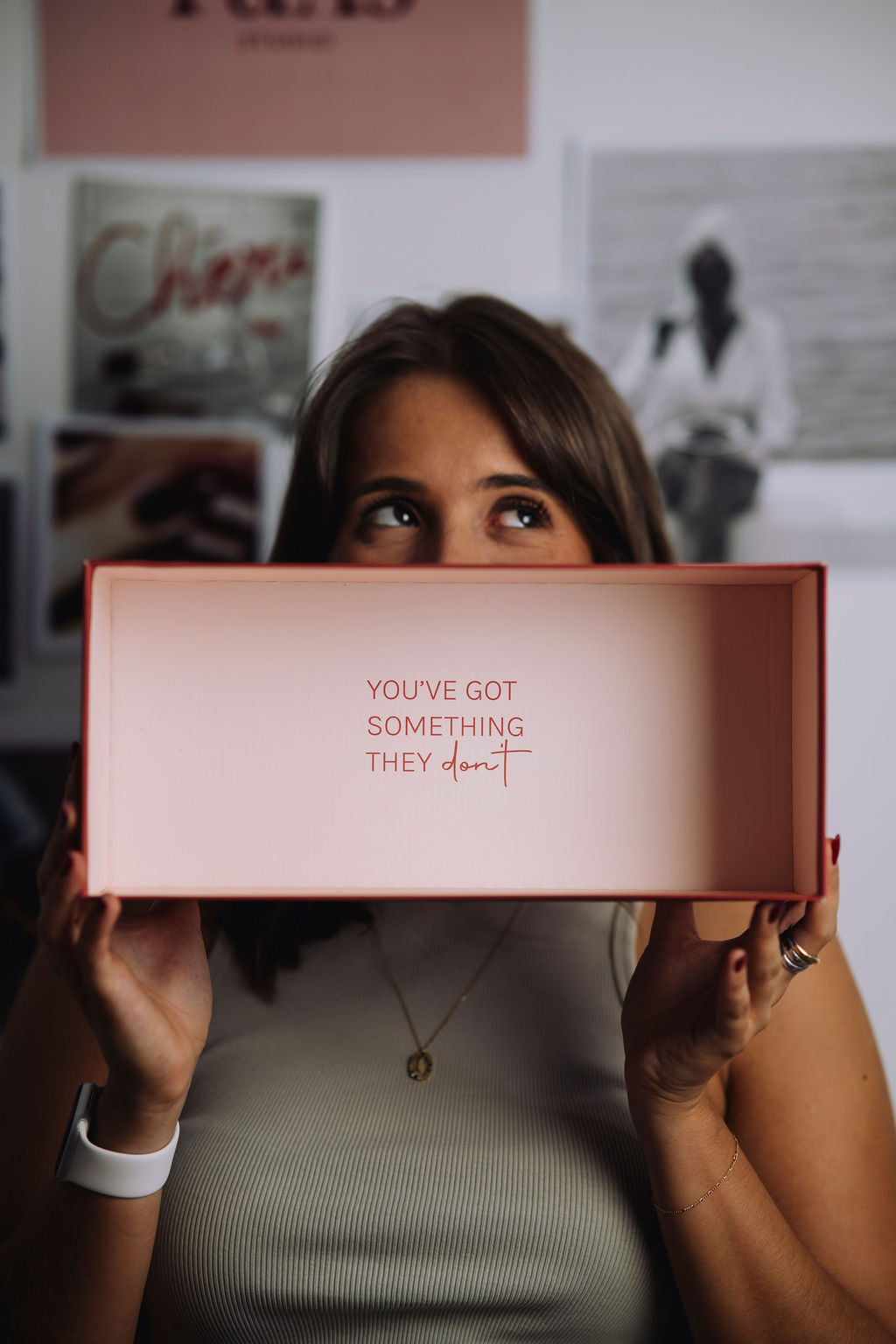 Person holding a pink box with text, standing in a room with posters on the wall.