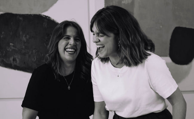 Two women laughing together in front of a laptop in an office setting.