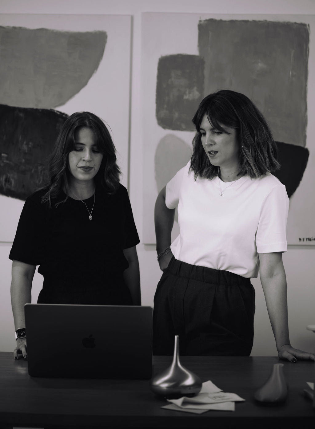 Two women looking at the computer with painting in the background