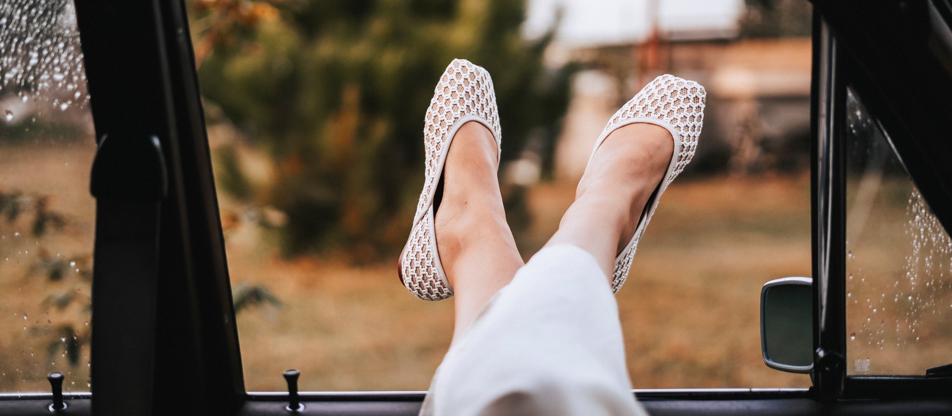 Feet in TUAS Louise shoes resting on a car dashboard with a blurred outdoor background