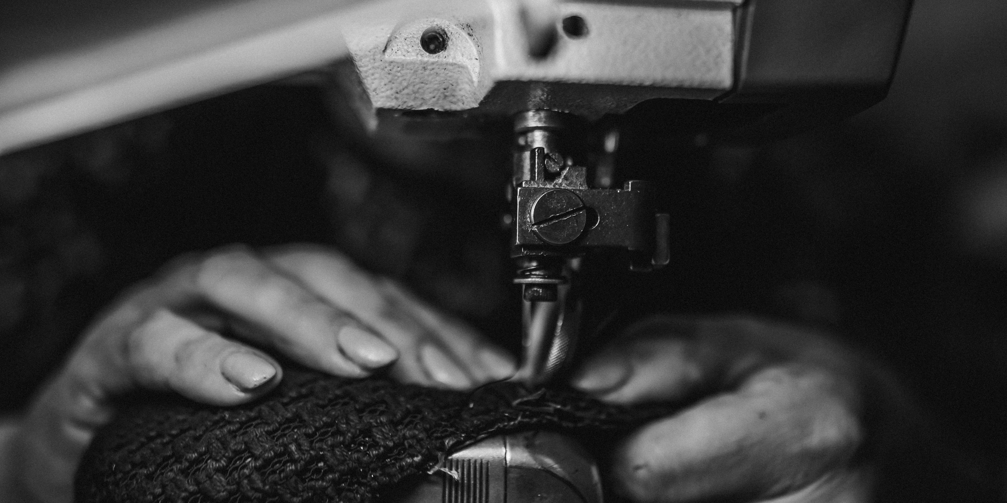 Close-up of hands using a sewing machine on a dark background