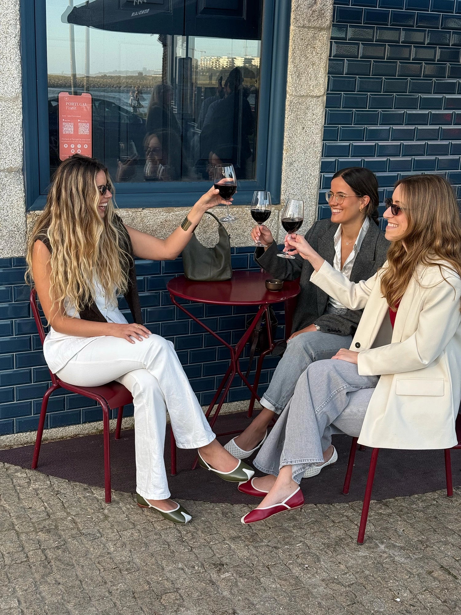Three women sitting outside a building, enjoying wine and conversation.