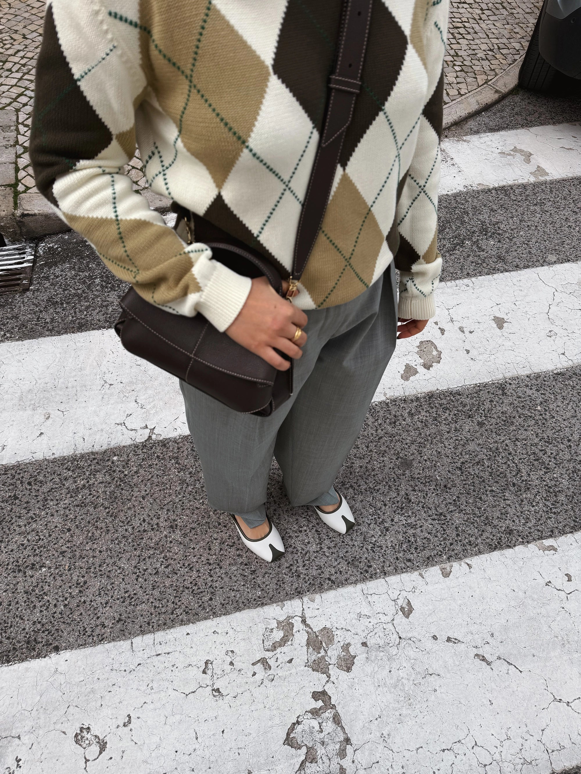 Person wearing a patterned sweater and holding a brown bag on a crosswalk
