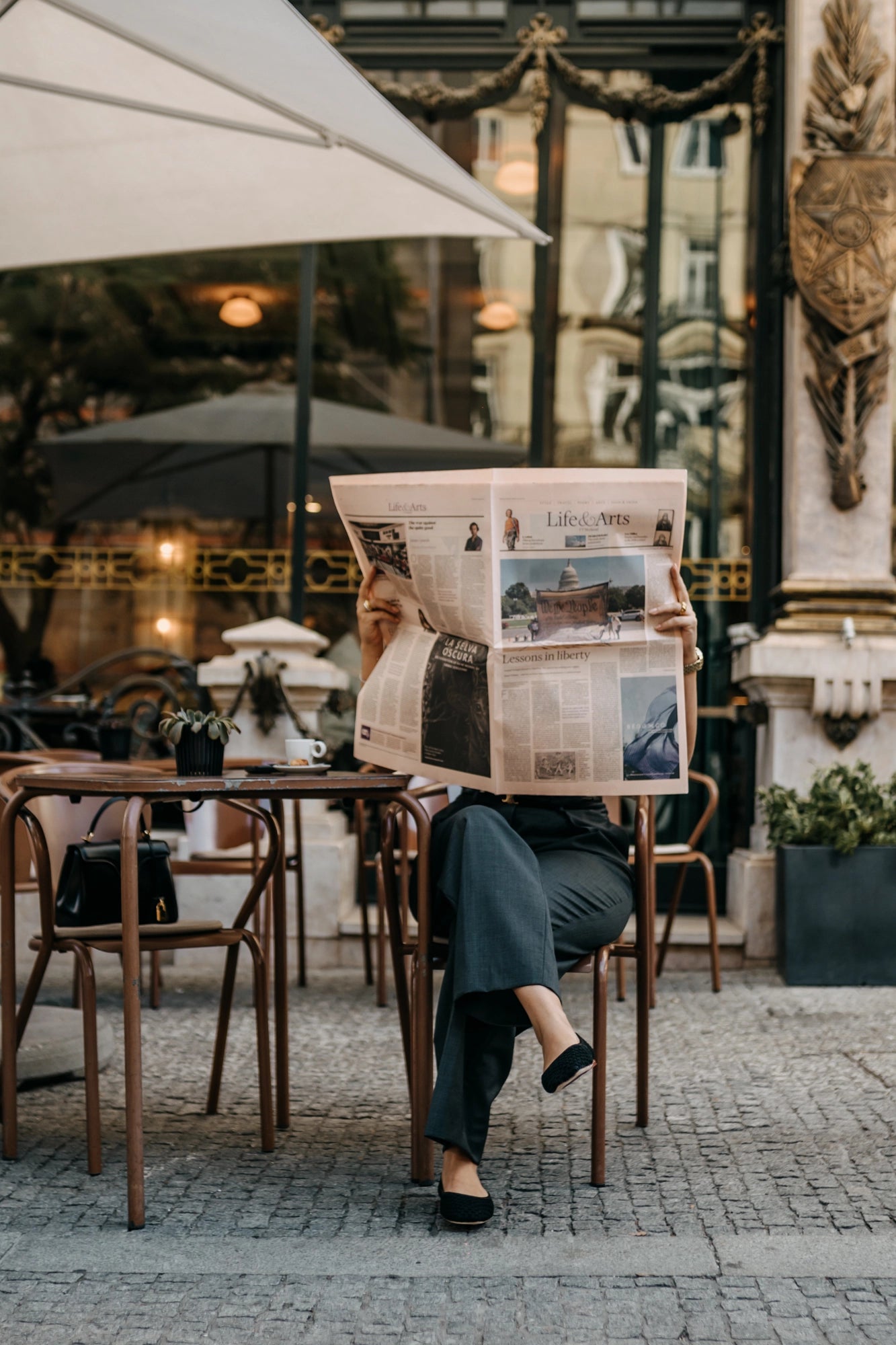 Person reading a newspaper outdoors at a cafe.