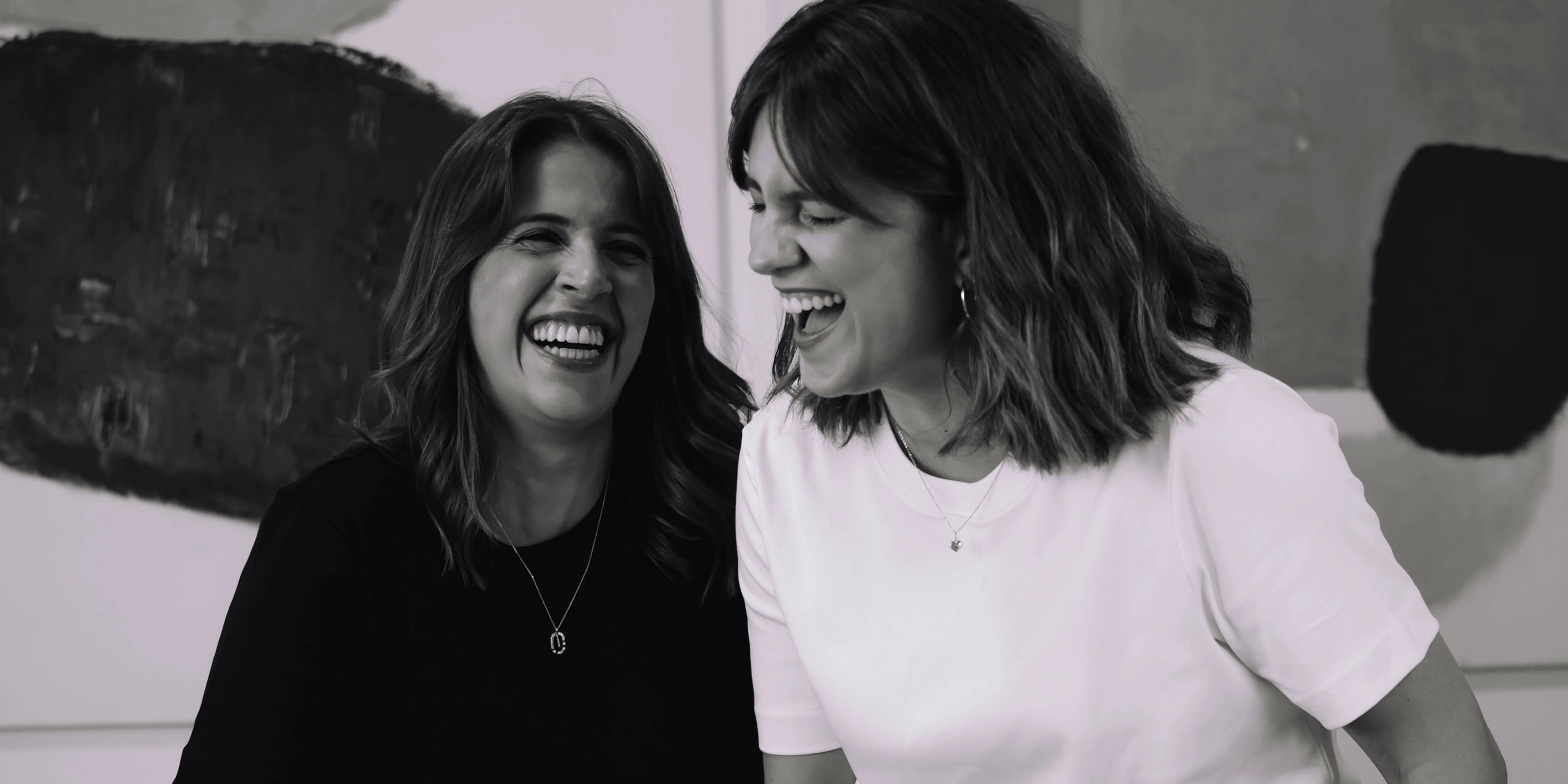 Two women laughing together in a black and white photo.