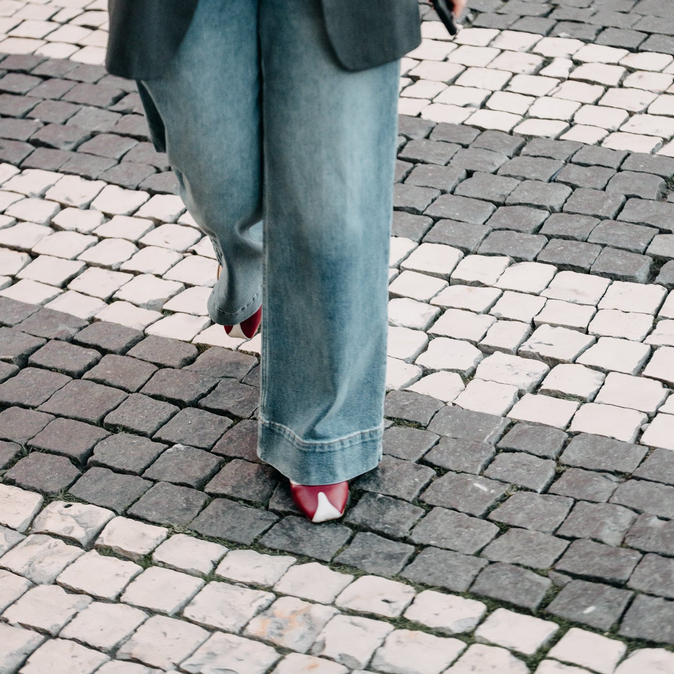 Person wearing a dark blazer and blue jeans on a cobblestone street