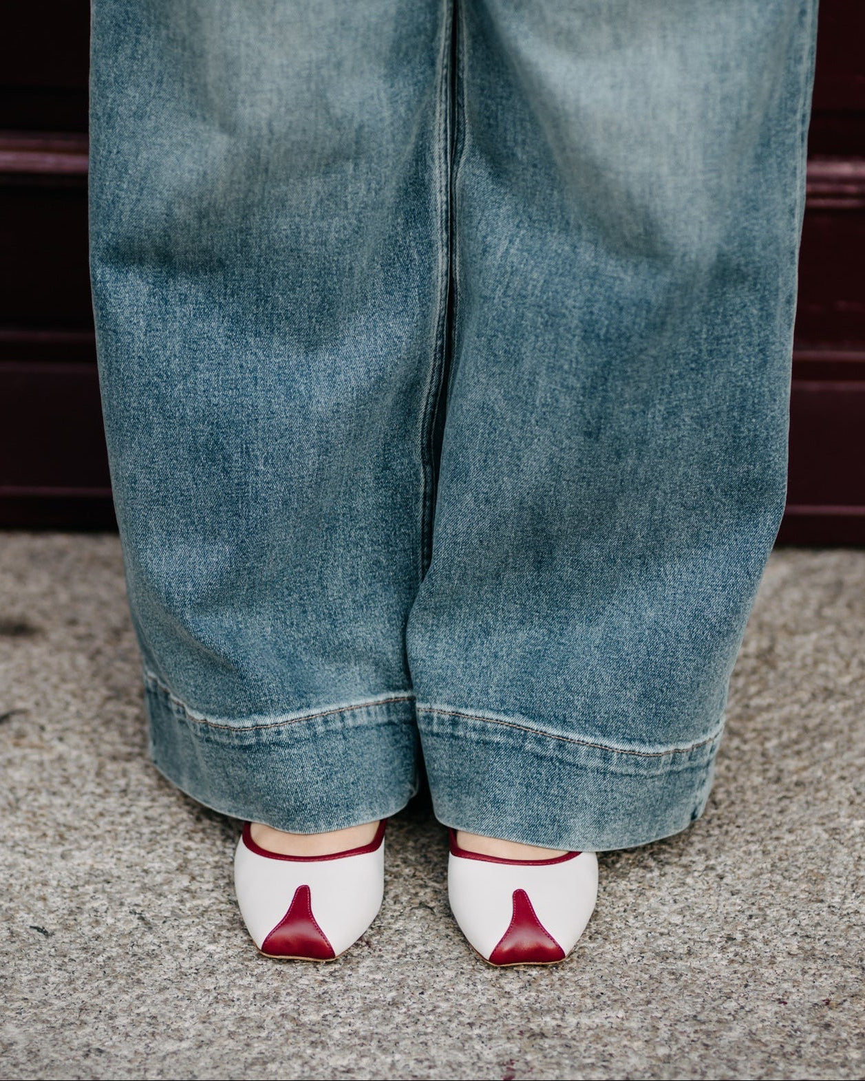 Person wearing blue jeans and white shoes with red accents on a neutral background