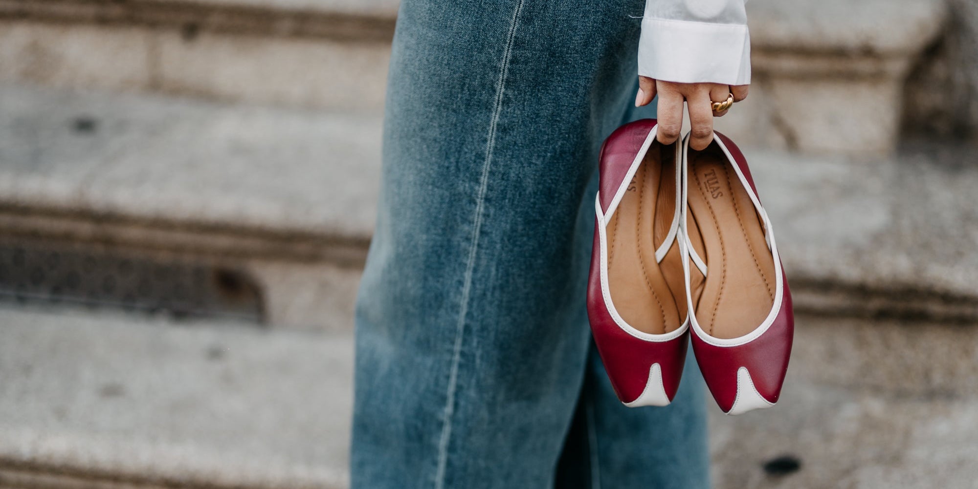 Red and white shoes held by a person wearing blue jeans on stone steps.