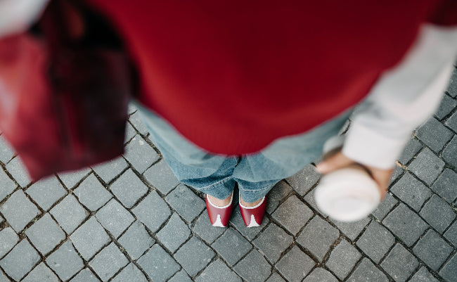 Person wearing a red jacket and blue jeans standing on a paved surface.