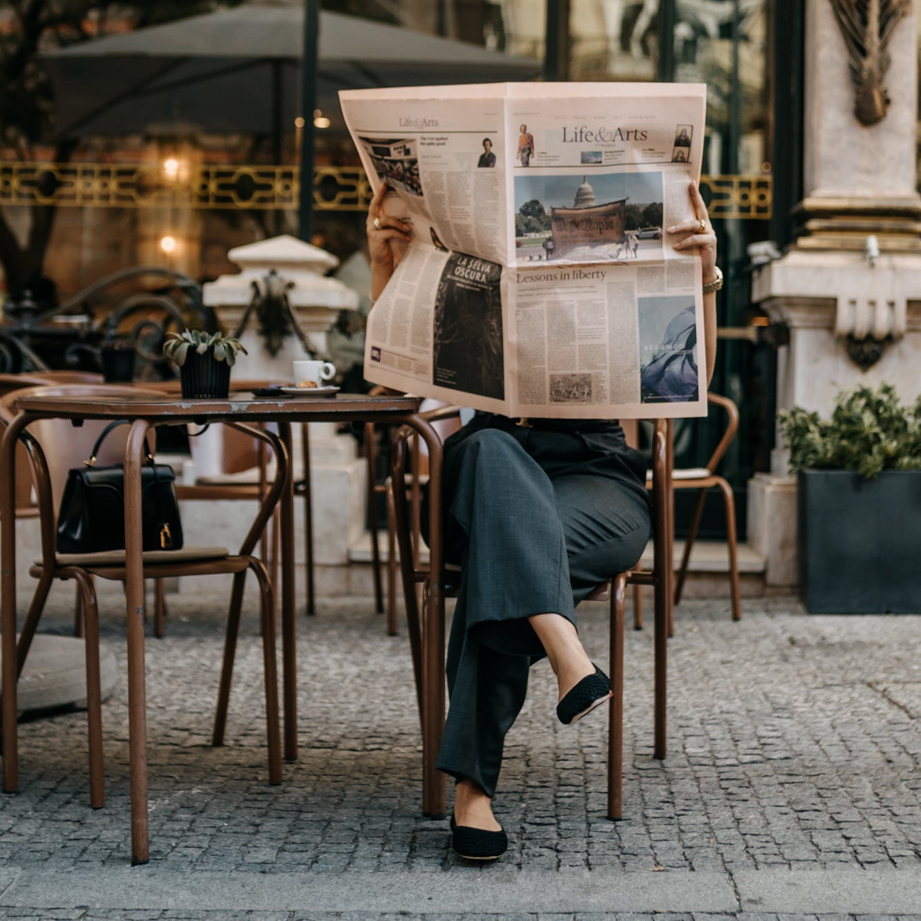 Person reading a newspaper outdoors at a cafe.