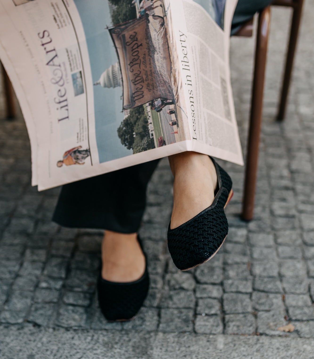 Person reading a newspaper with a visible photo of the Washington Monument on a cobblestone street.