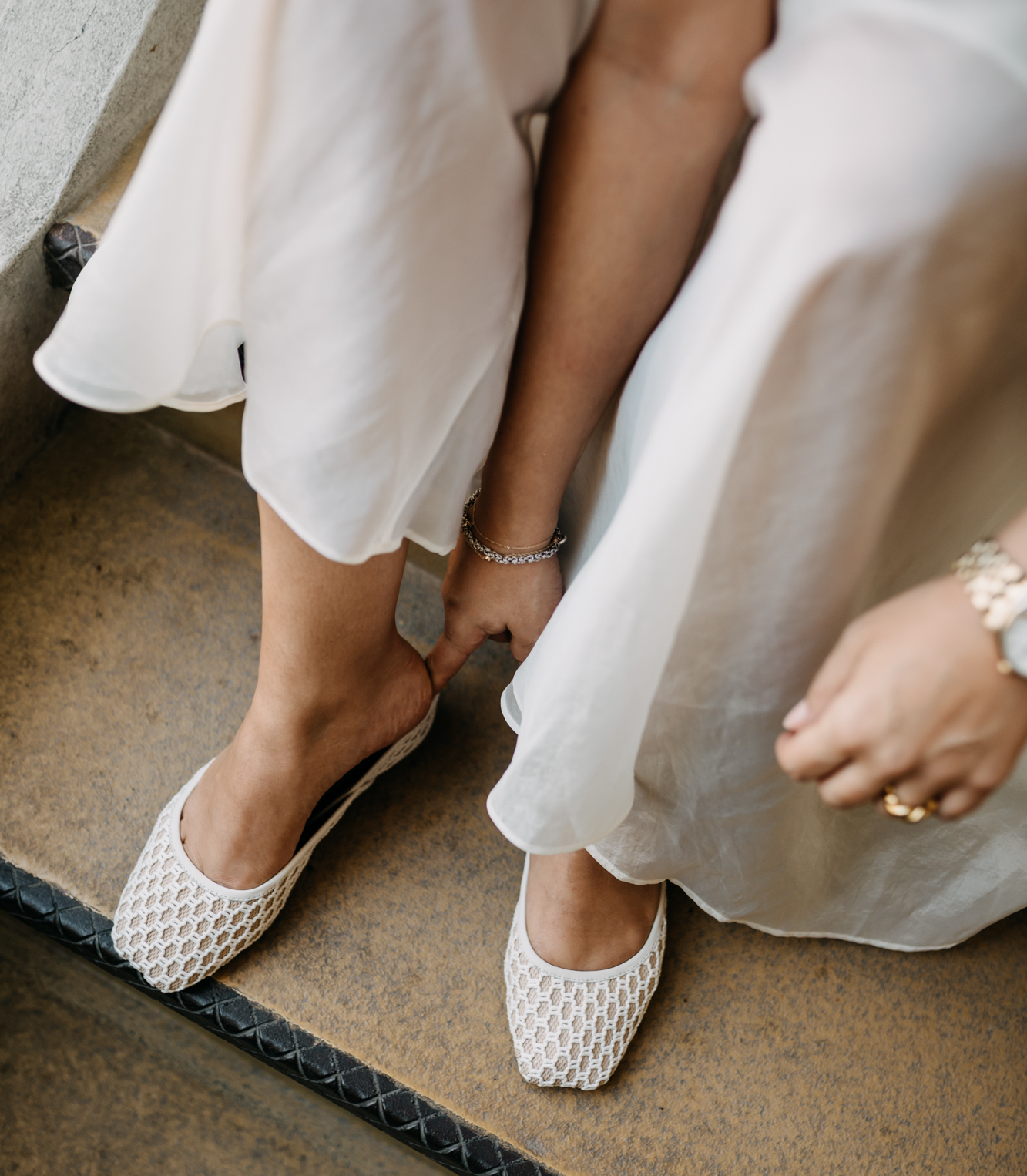 Close-up of two women in white shoes and dresses sitting on a step.