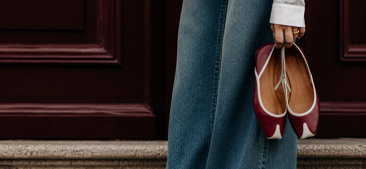 Person holding a pair of red shoes in front of a dark door.