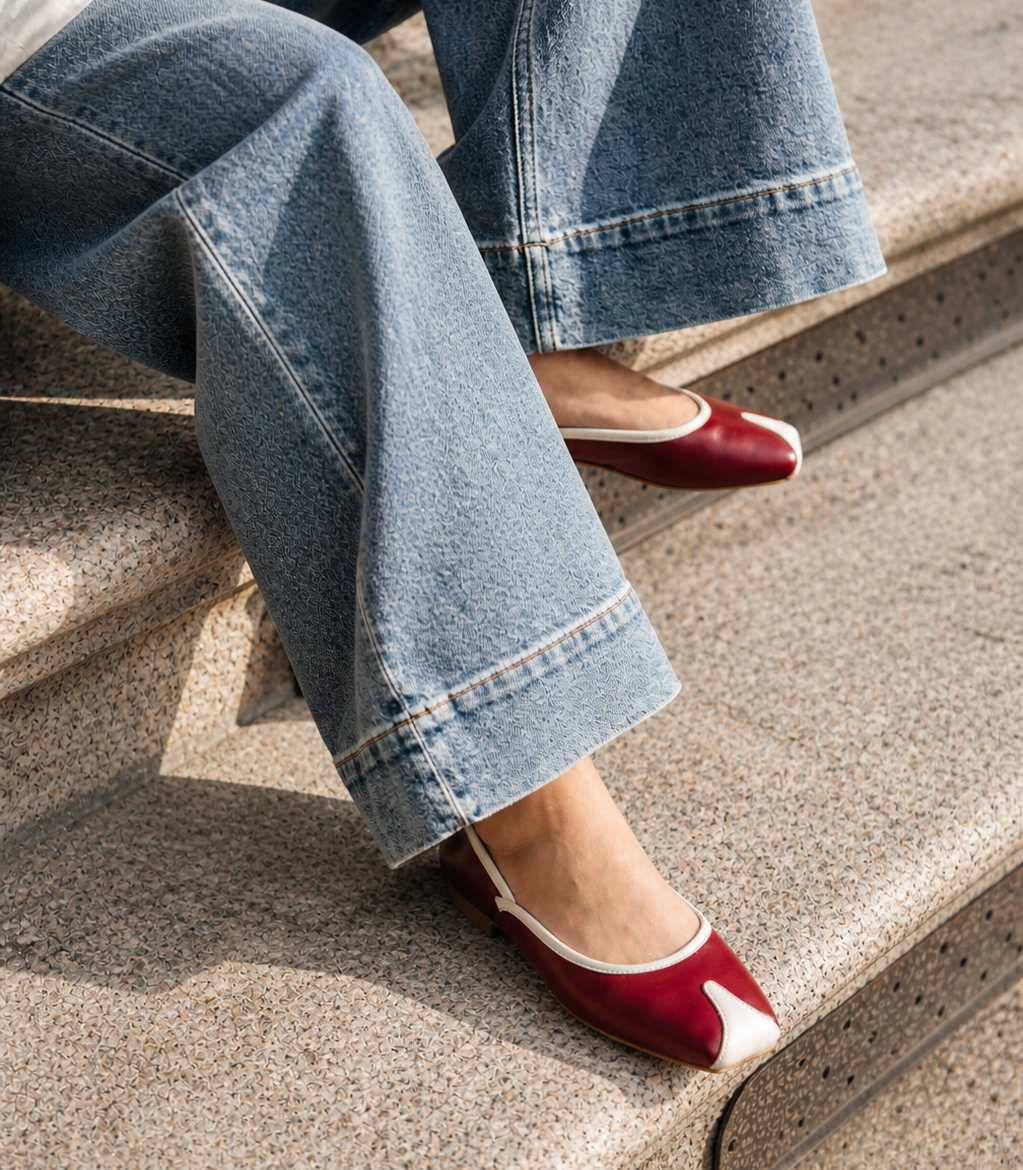 Person wearing blue jeans and red shoes sitting on a concrete step.