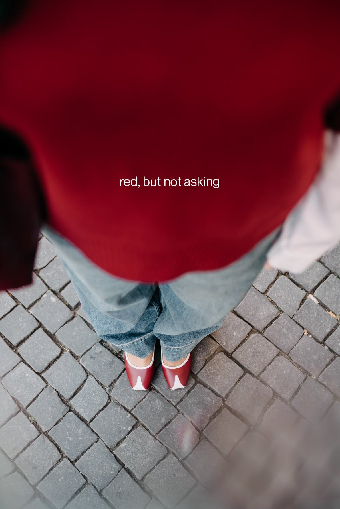Person wearing a red sweater and jeans standing on a paved surface with text 'red, but not asking'.