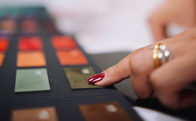 Close-up of a hand with red nail polish touching a color swatch card.