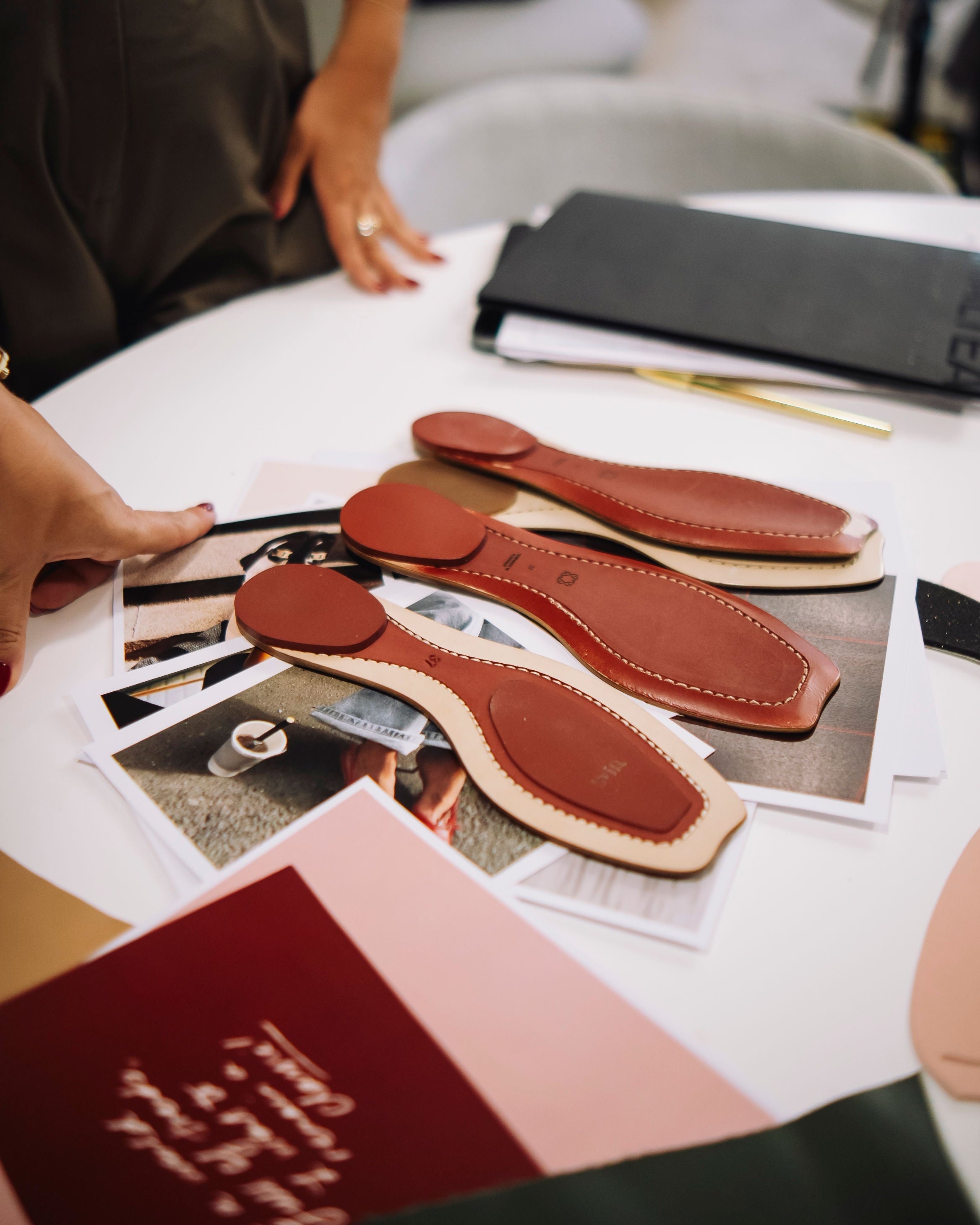 Close-up of leather insoles on a table with a person's hand reaching towards them.