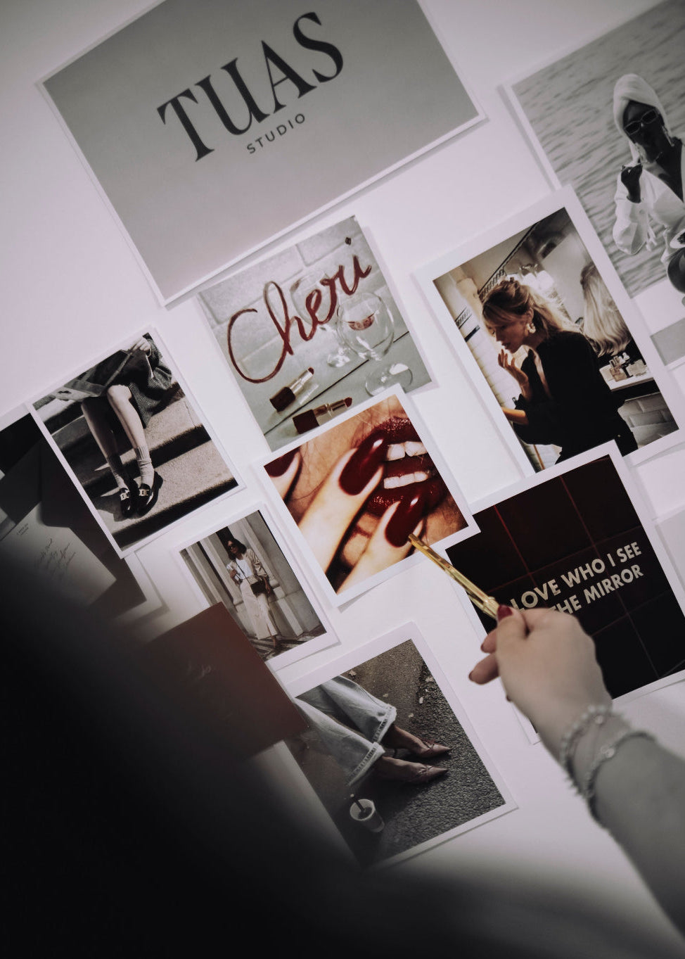 Collage of photos and text on a wall with a hand holding a book titled 'Over I See the Mirror'.