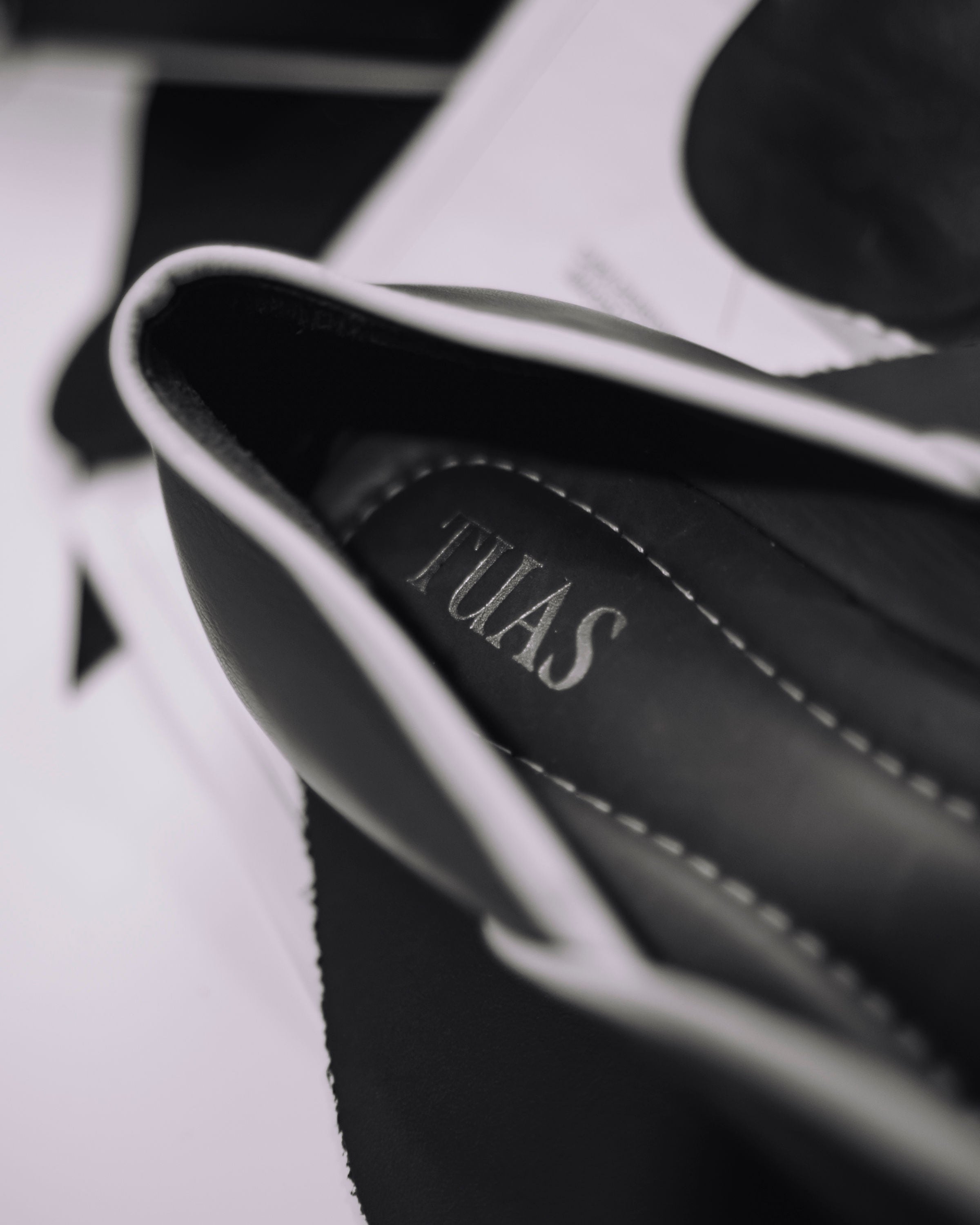 Close-up of a black leather bag with 'TUEAS' branding.