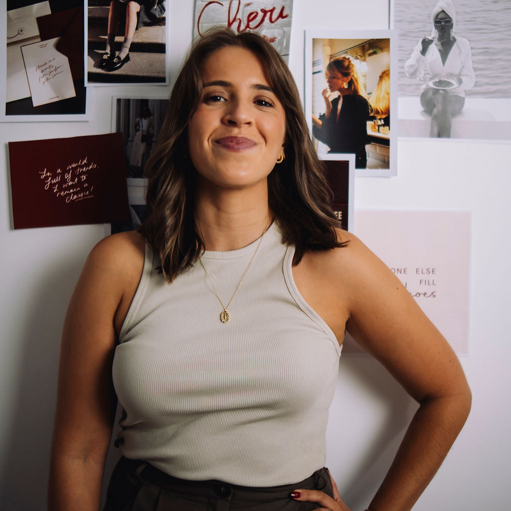 Woman standing in front of a wall with various photos and signs, including one that reads 'TUAS Studio'.