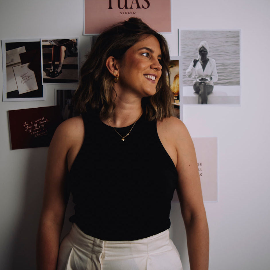 Woman standing in front of a wall with various posters, including one with the word 'TUAS'.