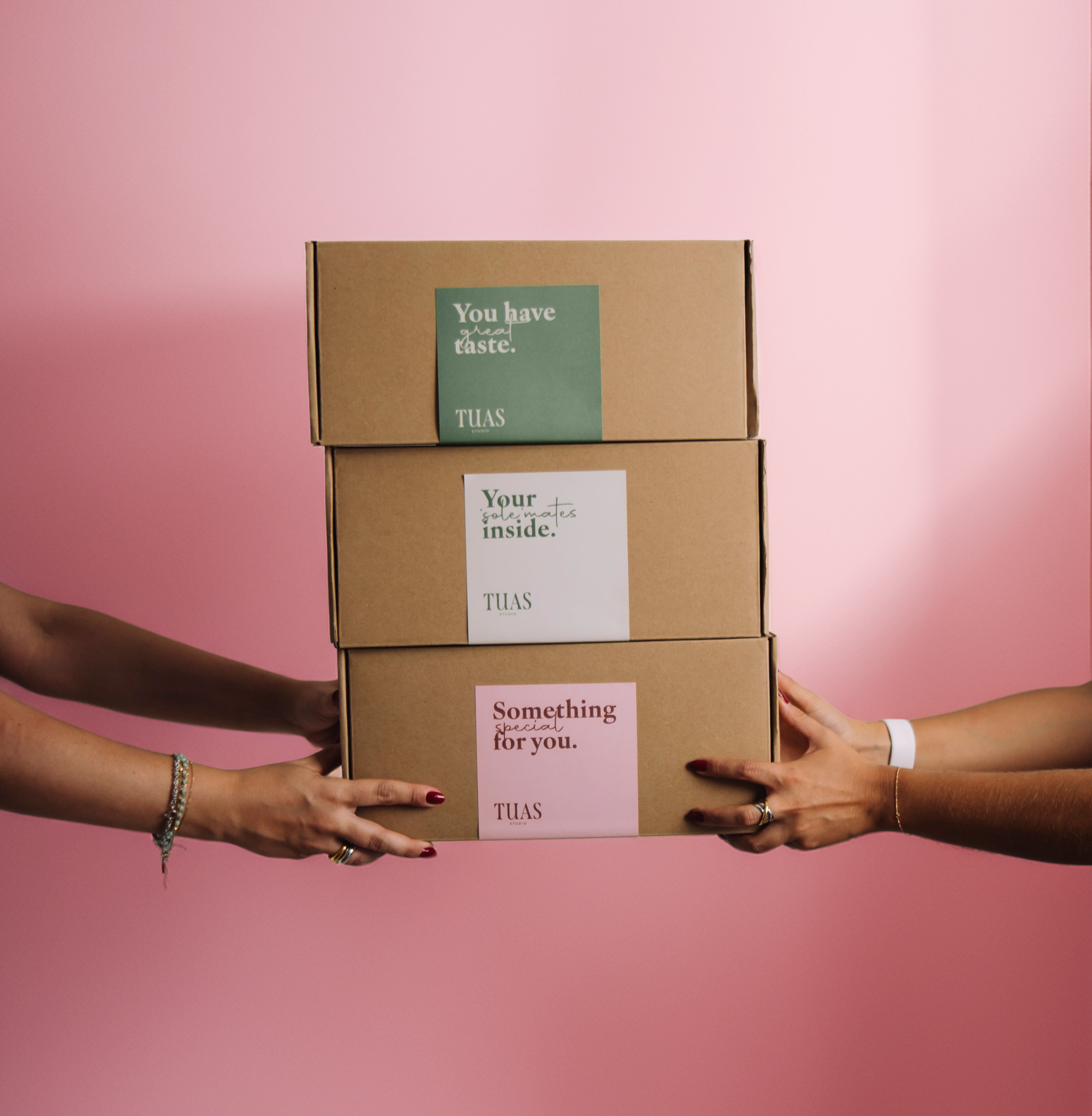 Two hands reaching towards a stack of three cardboard boxes with text on a pink background