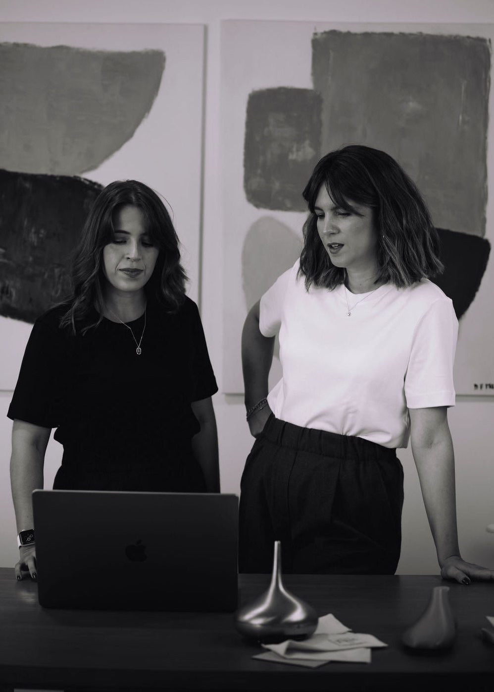 Two women looking at the computer with painting in the background