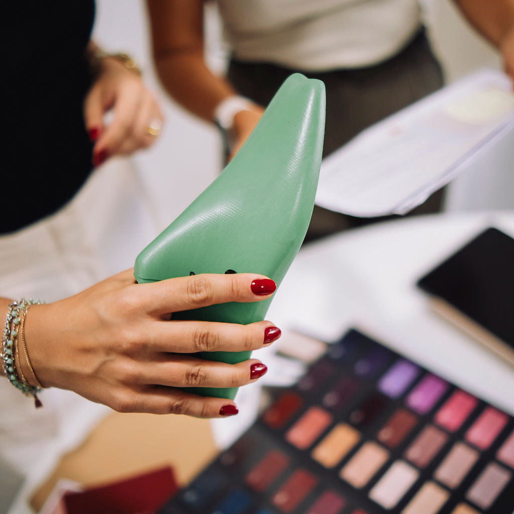 Person holding a green makeup product with a color swatch palette in the foreground