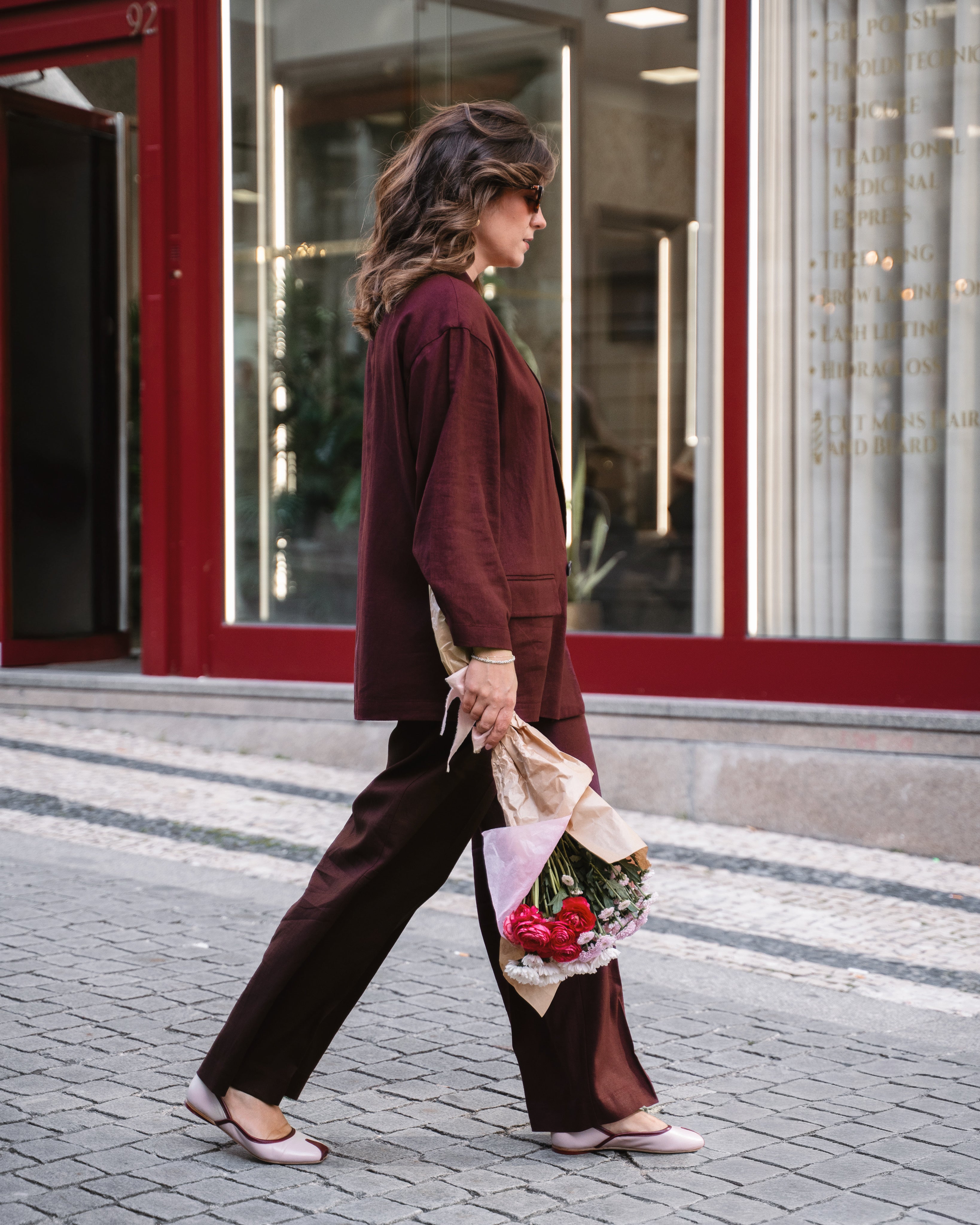 Woman walking outdoors holding a floral arrangement, with a building in the background.