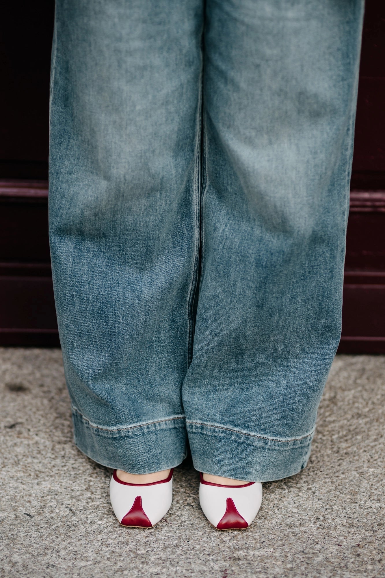 Person wearing blue jeans and white shoes with red accents on a concrete surface.