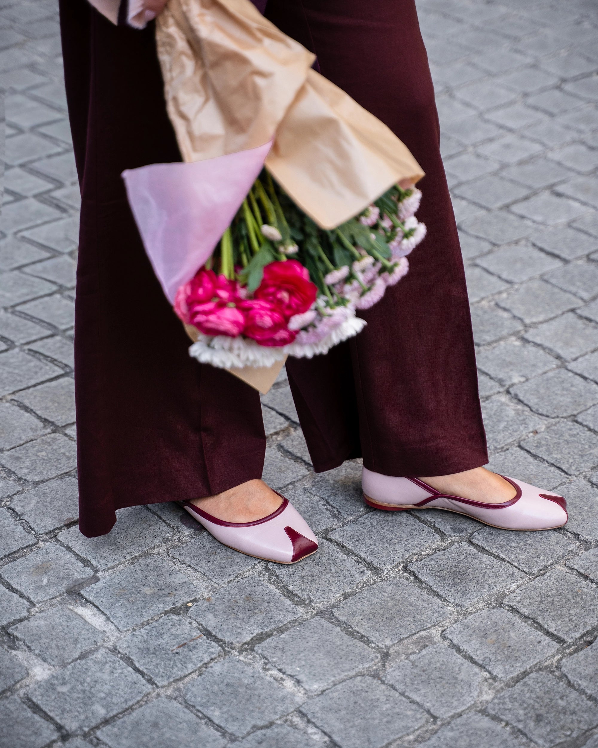 Person holding a bouquet of flowers and a bag on a paved street.