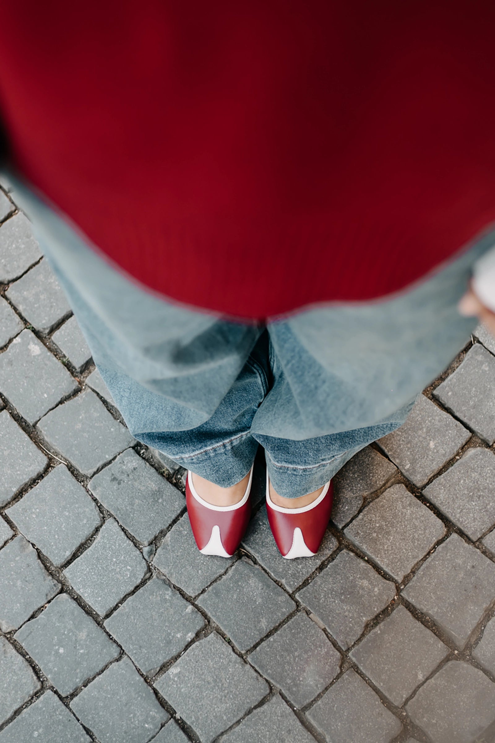 Person wearing red shoes and blue jeans standing on a paved surface