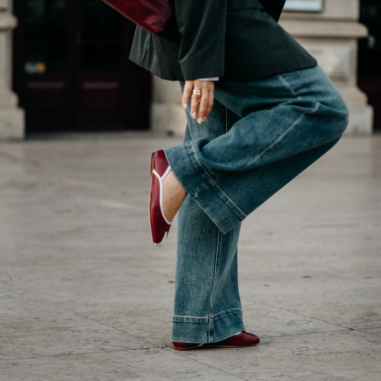 Person wearing a dark green coat, blue jeans, and red shoes on a city street.