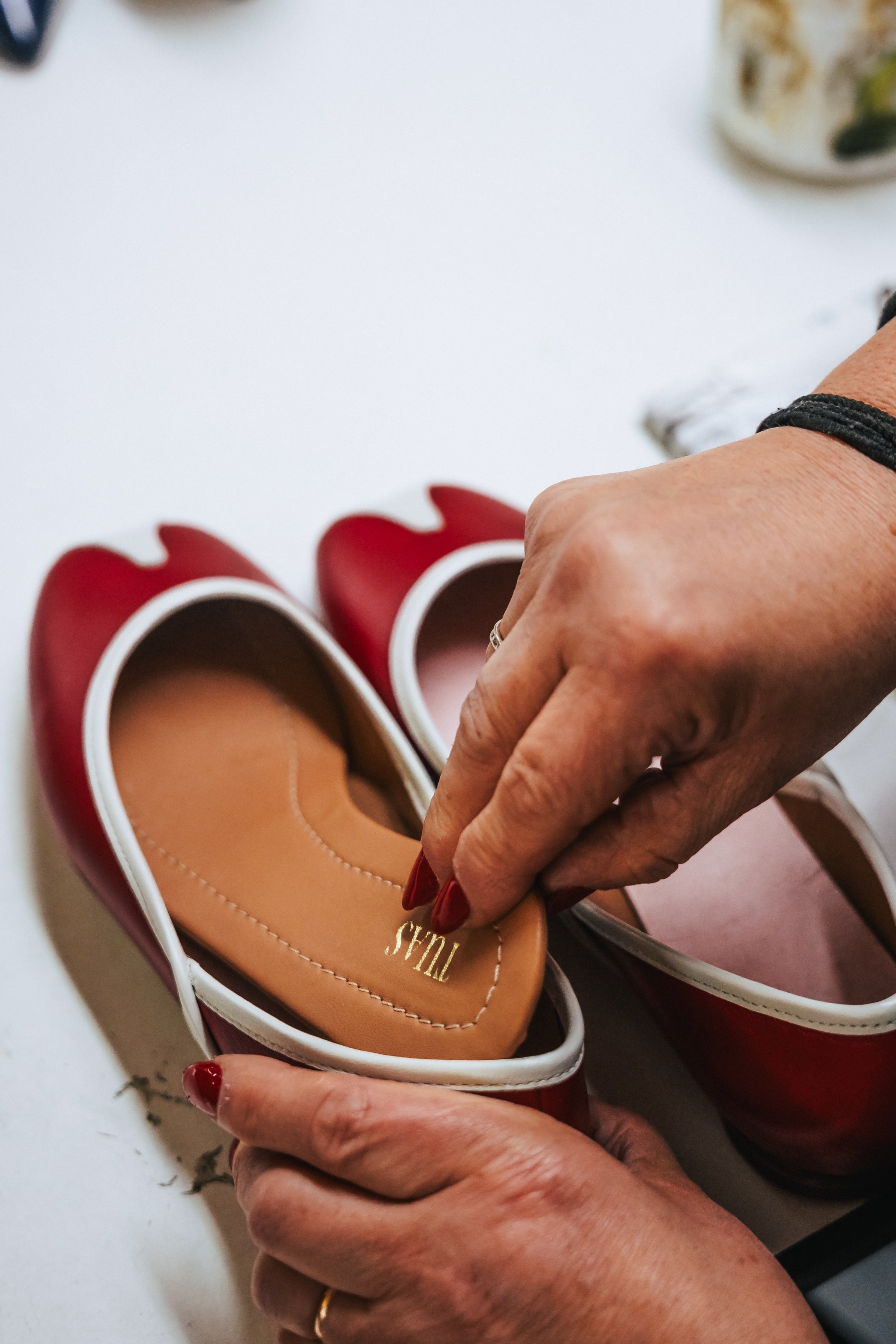 Red shoes with a visible brand logo being held by a person on a white surface.