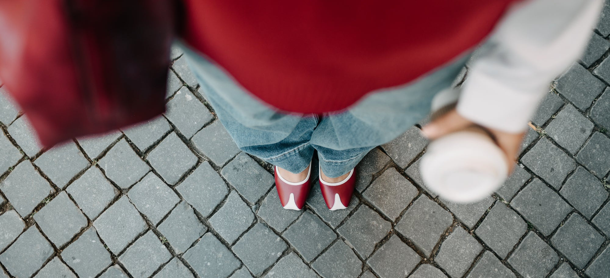 Person wearing a red sweater and blue jeans standing on a paved surface.