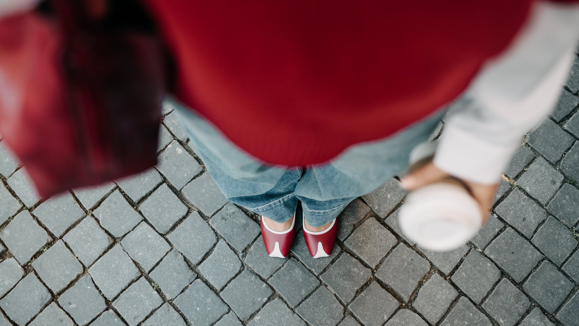 Person wearing a red sweater and blue jeans standing on a paved surface.