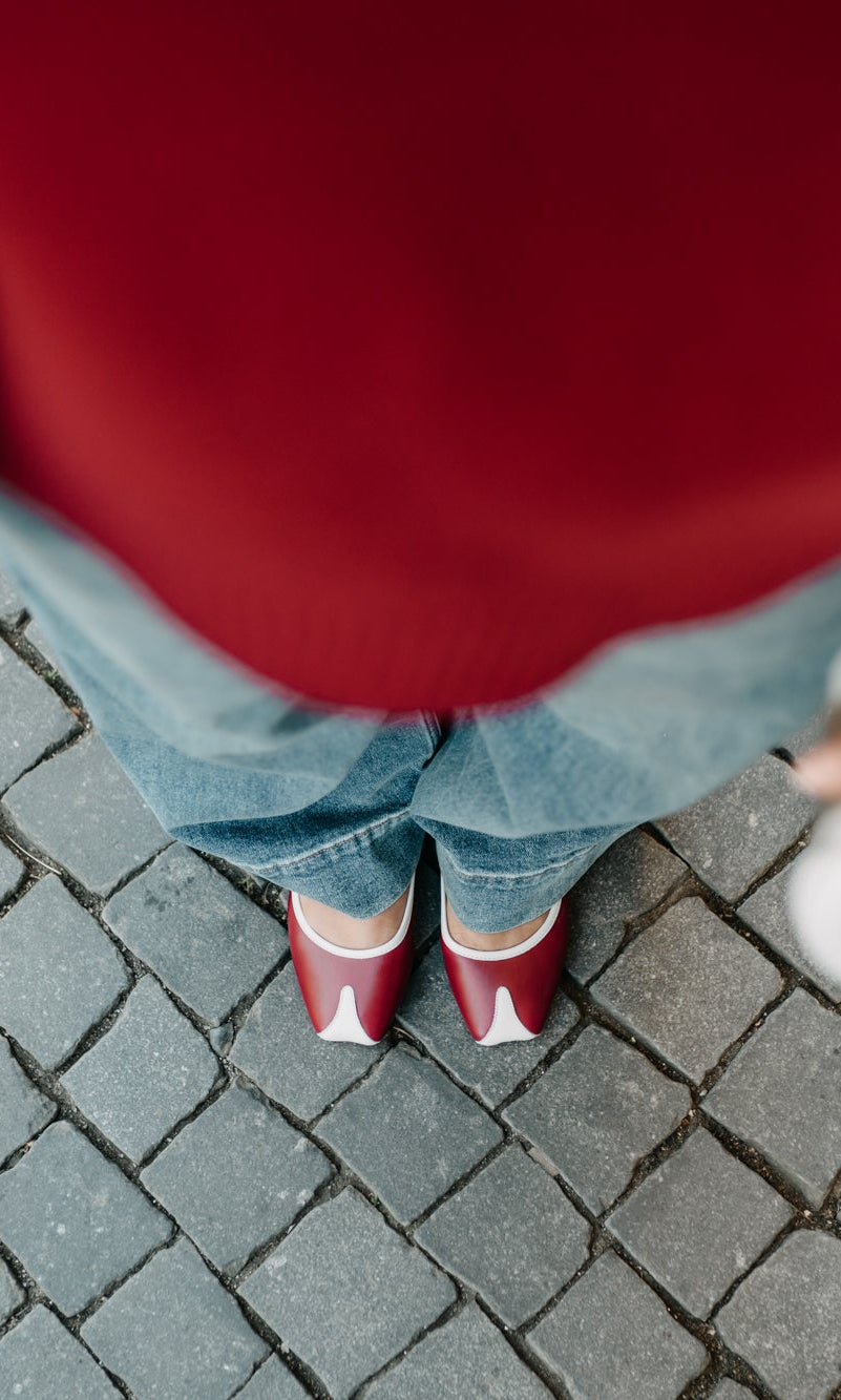 Person wearing a red sweater and blue jeans standing on a paved surface.