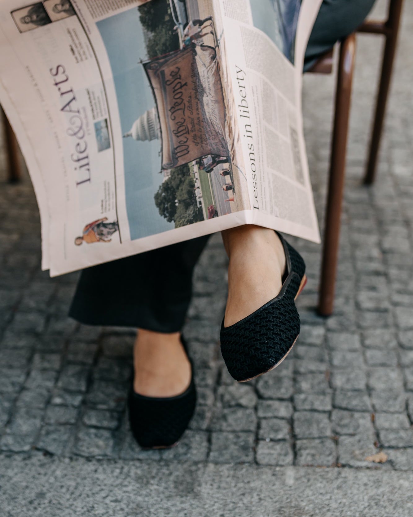 Person reading a newspaper with a visible photo of the Washington Monument on a cobblestone street.