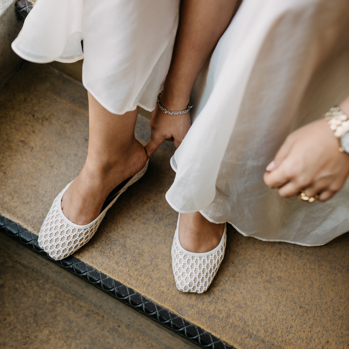Close-up of a women in white flat TUAS shoes and dresses sitting on a step.