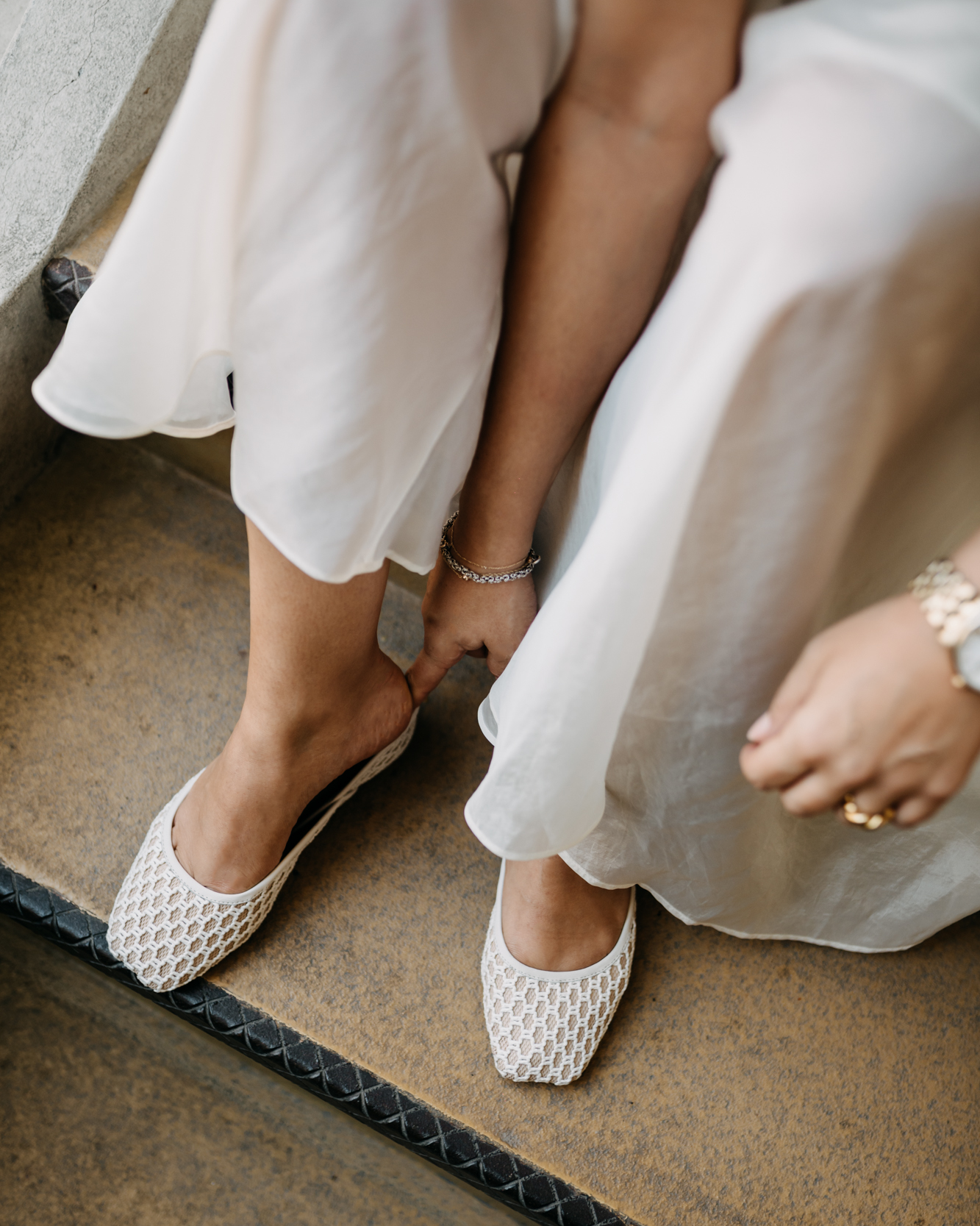 Close-up of two women in white shoes and dresses sitting on a step.