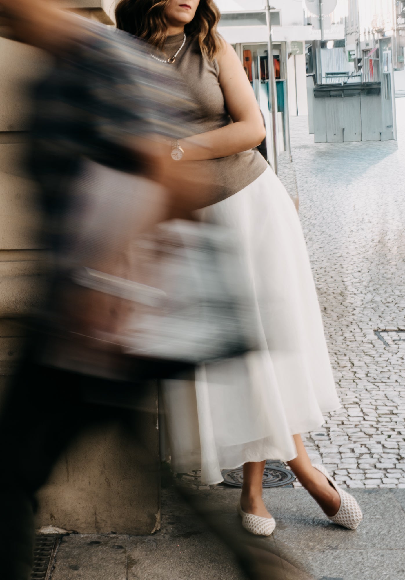 Woman in a sleeveless top and white skirt standing on a street, with blurred motion effect.
