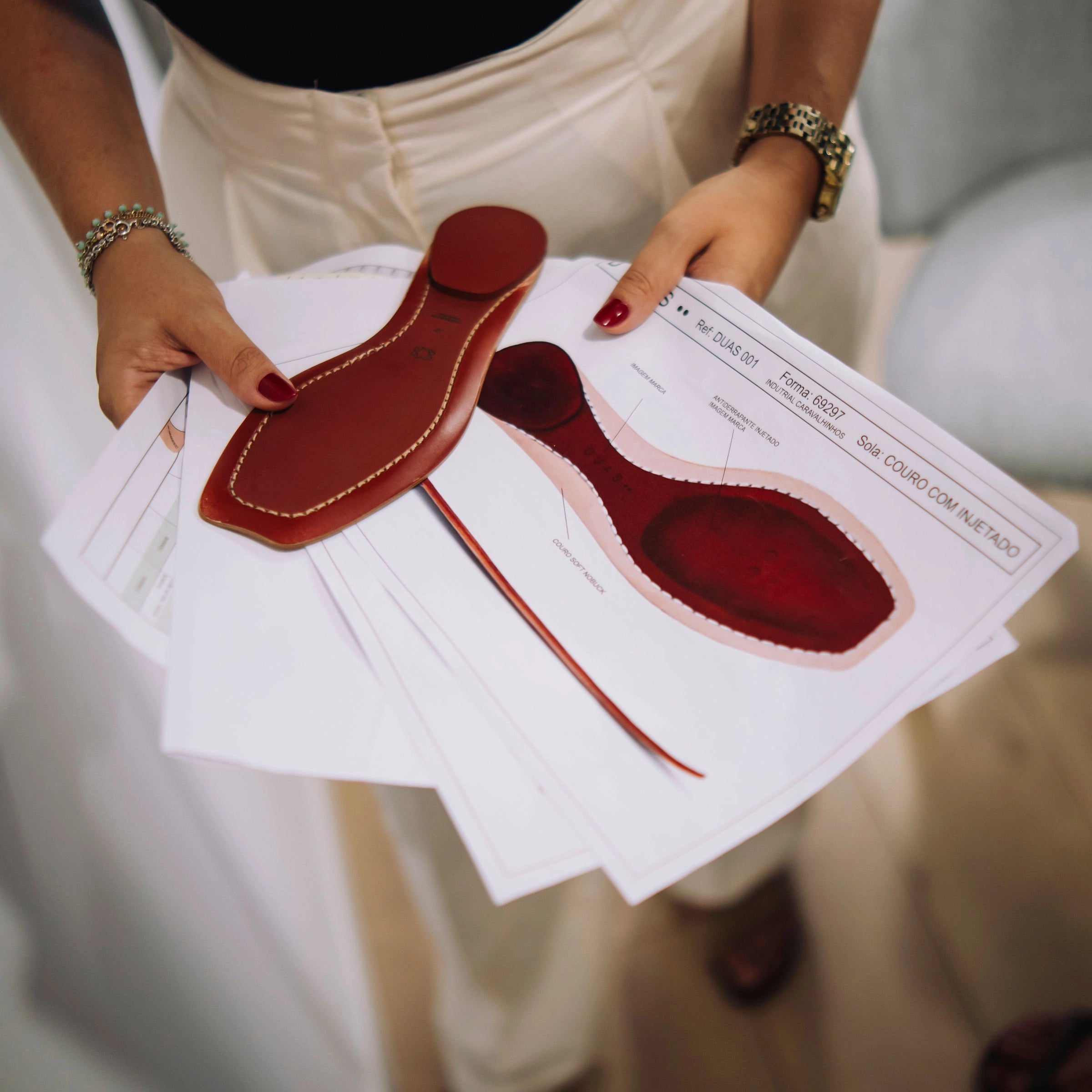 Person holding red leather shoe lasts and a diagram on white paper.